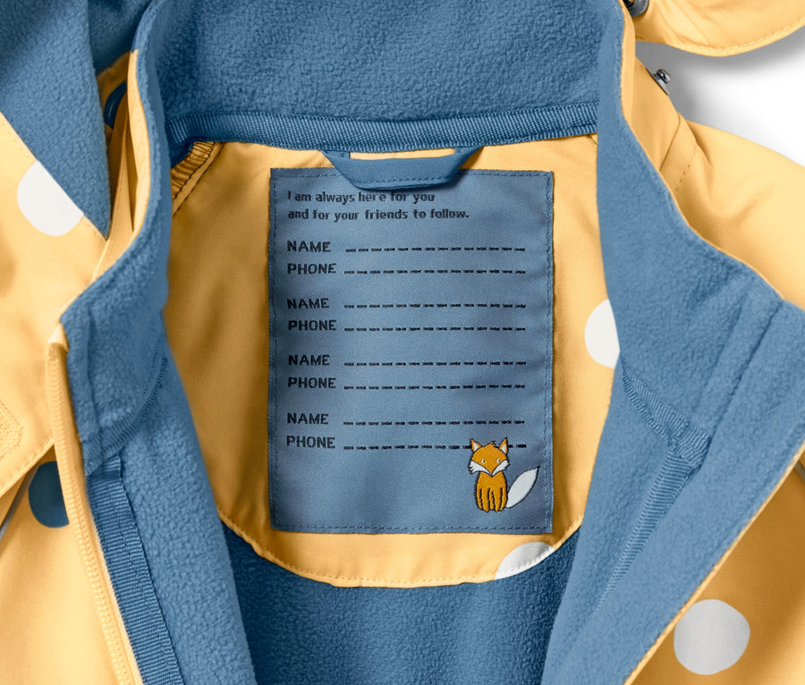 Détail d'une combinaison softshell pour enfant avec un imprimé intégral à pois et une étiquette pour le nom et le numéro de téléphone.