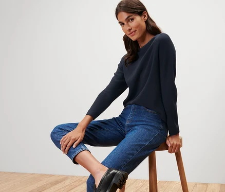 Femme assise sur un tabouret portant un pull en maille bleu foncé.