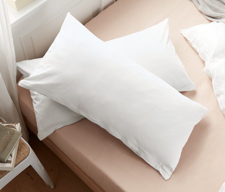 Deux taies d’oreiller en jersey blanc cassé sont posées sur un lit.