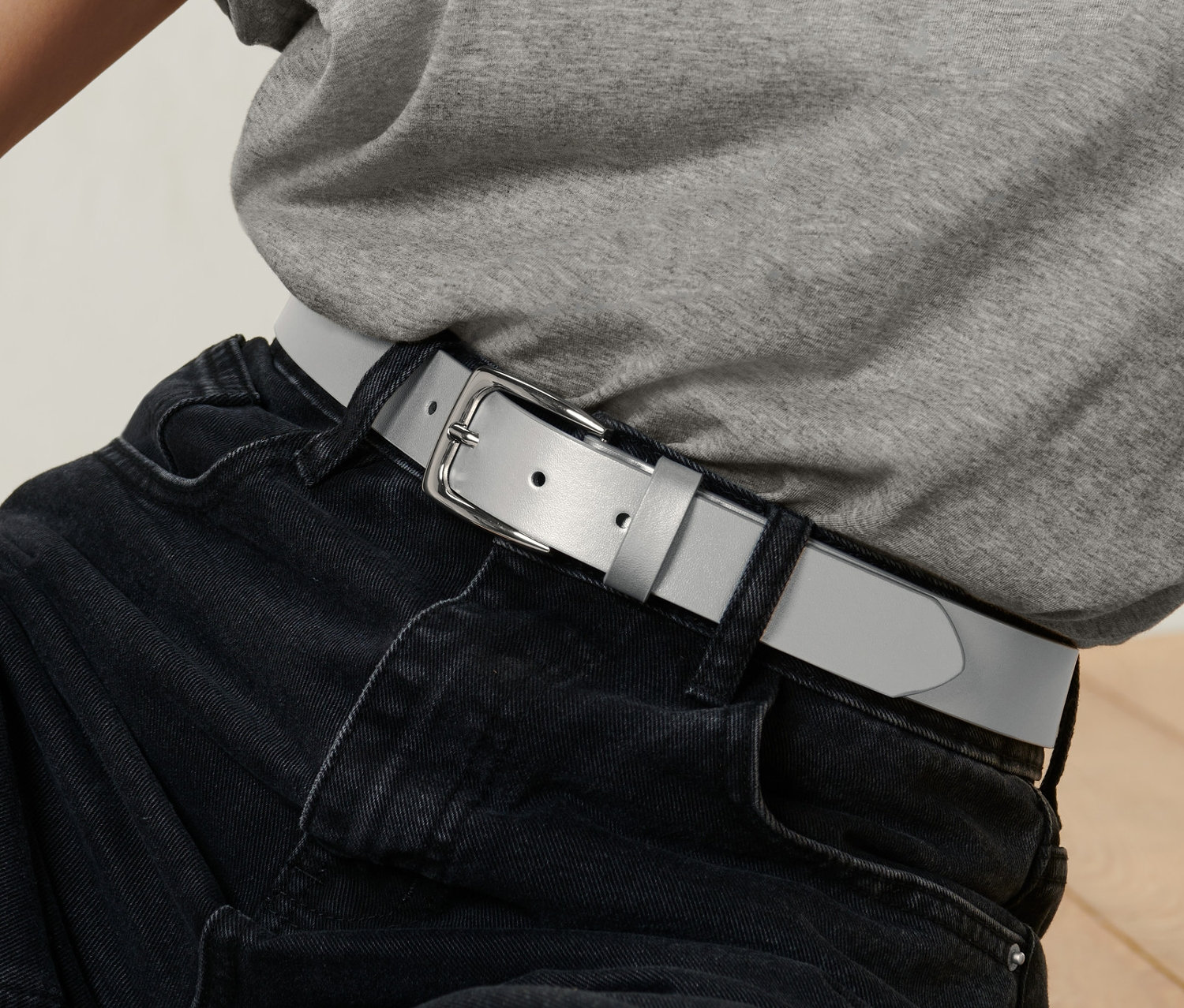 Une personne porte un t-shirt gris et un jean noir avec une ceinture grise.