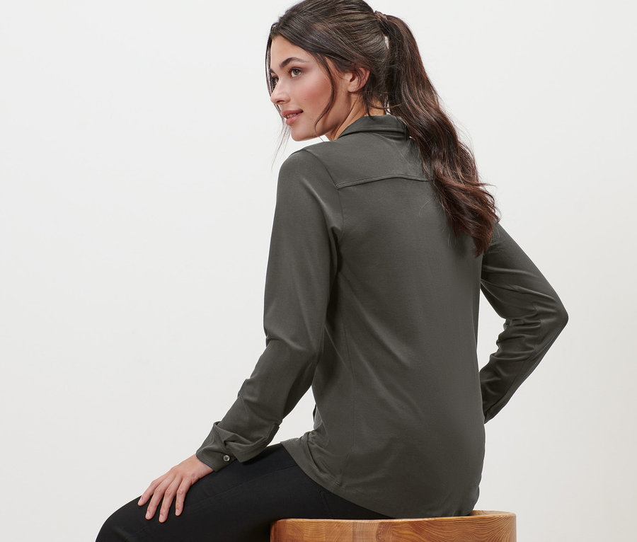 Femme assise sur un tabouret portant une blouse avec patte de boutonnage.