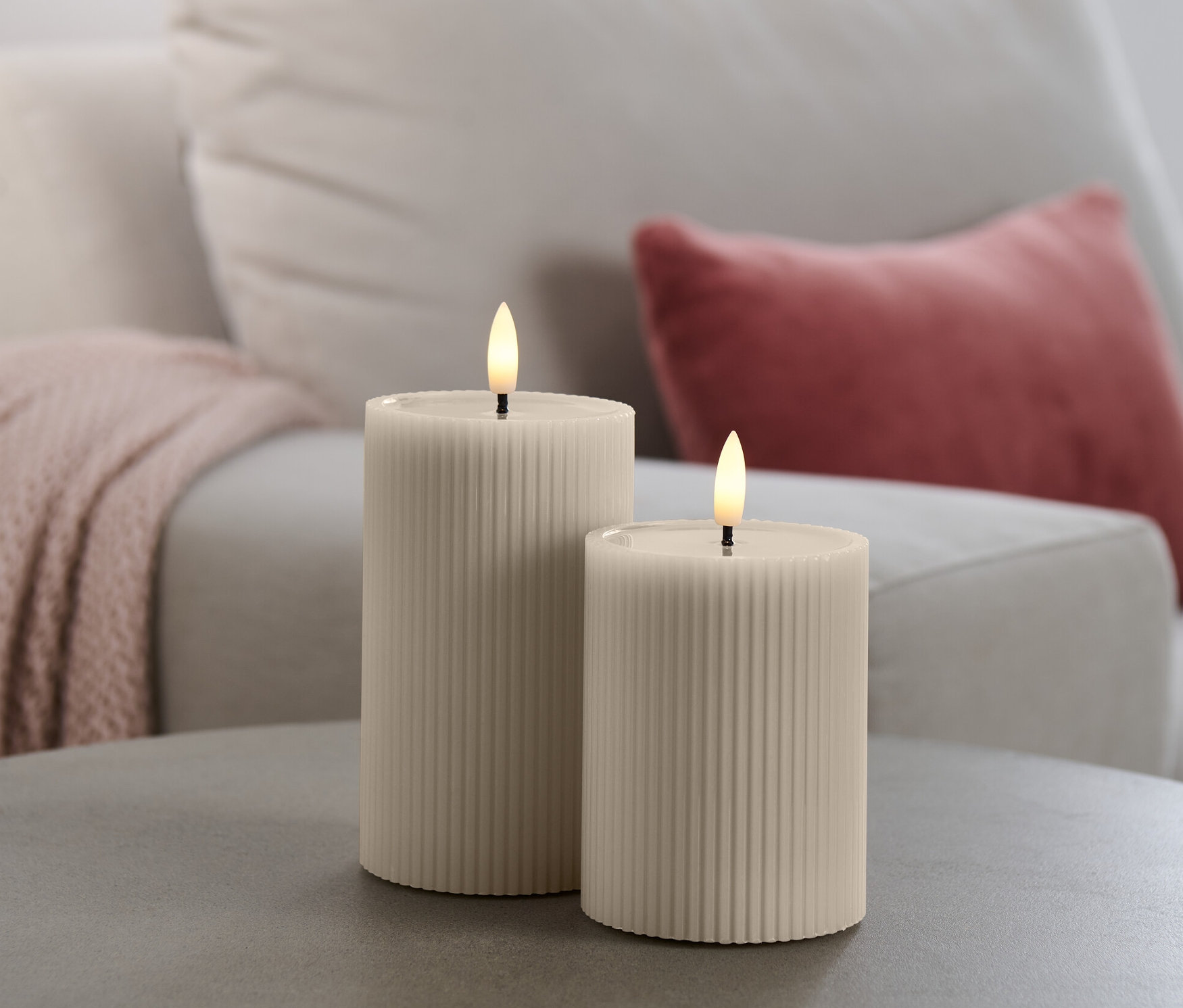 Deux bougies à LED avec miroir en cire véritable sur une table grise, avec un canapé en arrière-plan.
