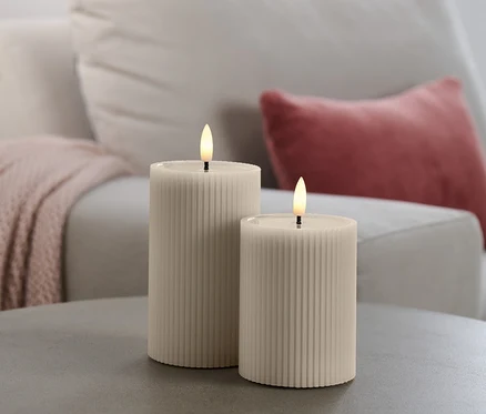 Deux bougies à LED avec miroir en cire véritable sur une table grise, avec un canapé en arrière-plan.