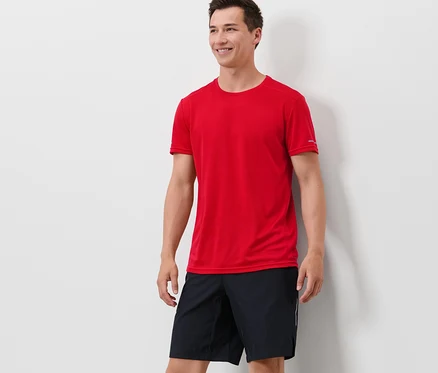 Un homme debout portant un t-shirt technique rouge et un short noir.