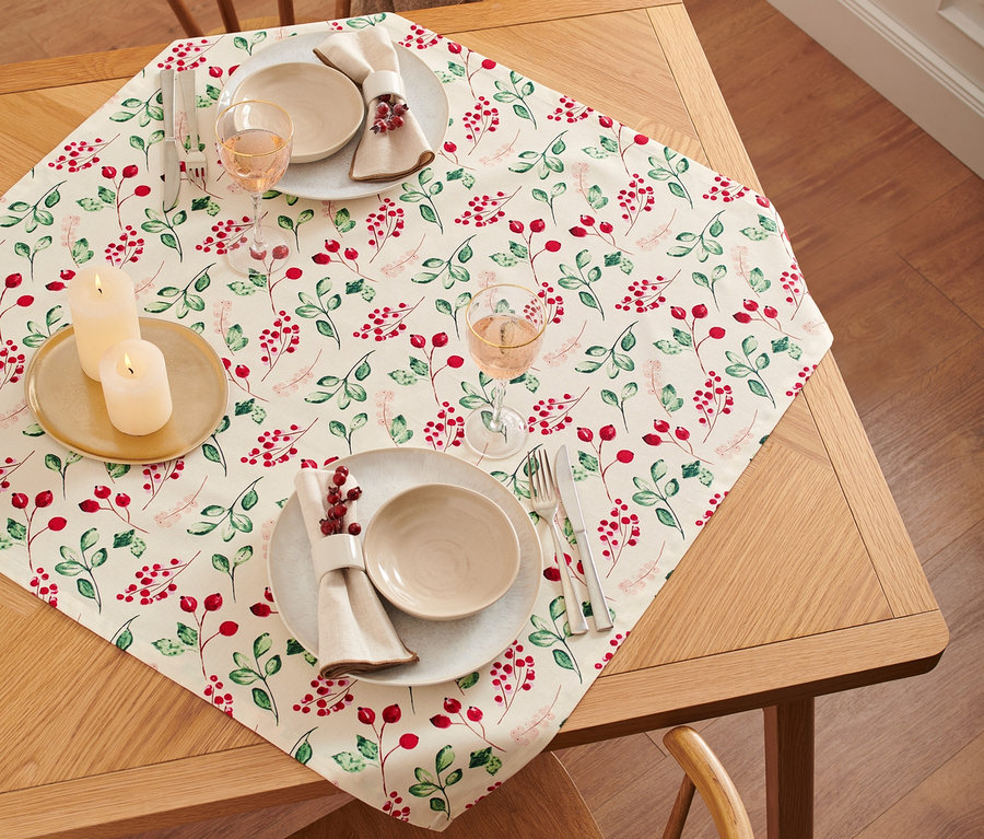 Une nappe en coton à motif végétal rouge est posée sur une table en bois avec des assiettes, des couverts et des verres.