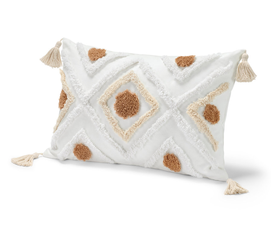 Un coussin décoratif d'environ 40 x 60 cm, blanc avec des motifs marrons et blancs et des pompons aux coins.