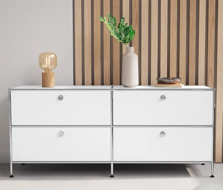 Un meuble bas en métal « CN3 » blanc avec 4 tiroirs et une lampe de table en bois sont placés l'un à côté de l'autre.