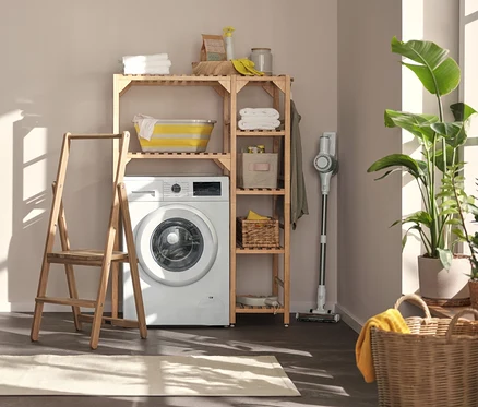 Dans la buanderie, il y a une machine à laver, au-dessus une étagère à machine à laver avec élément latéral et à gauche un escabeau en bois massif.