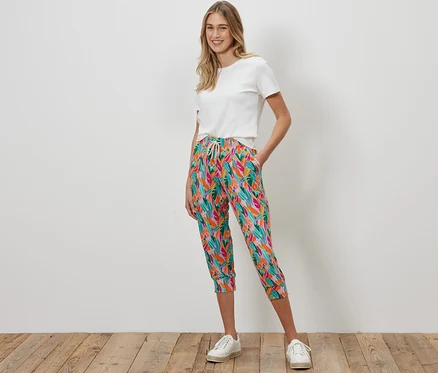Une femme debout porte un pantalon 3/4 en jersey multicolore et un t-shirt blanc.