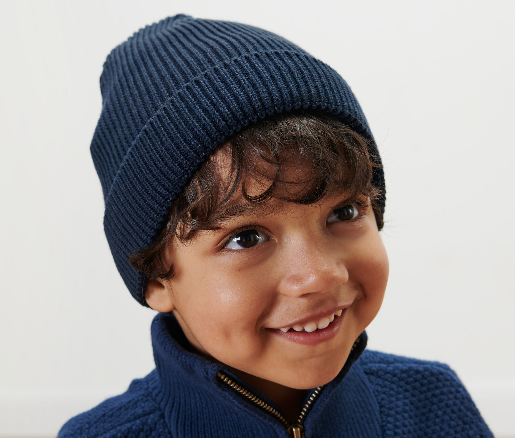 Un garçon souriant porte un bonnet en maille pour enfant bleu.