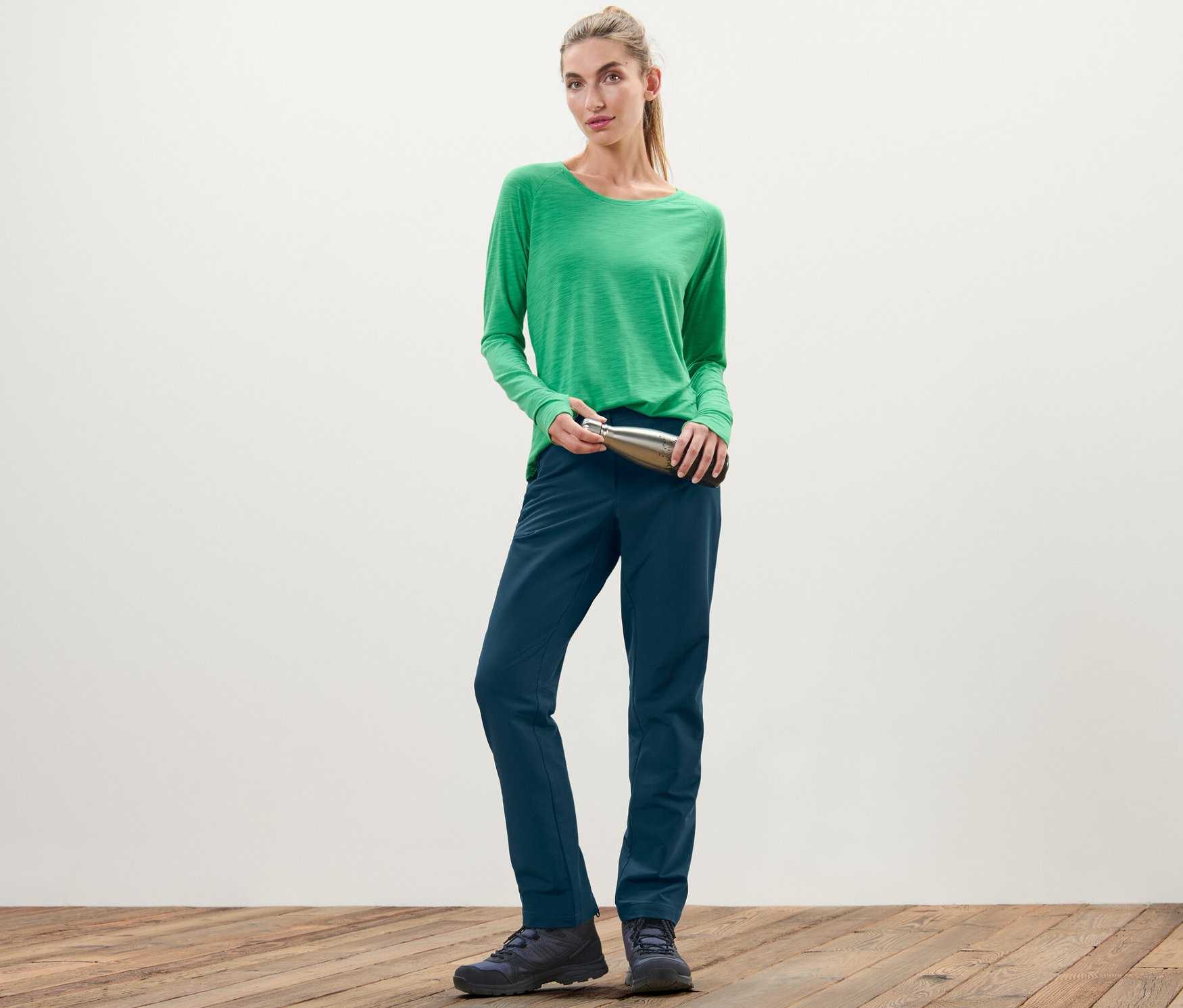 Une femme portant un t-shirt vert tient une bouteille argentée et porte un pantalon en softshell.