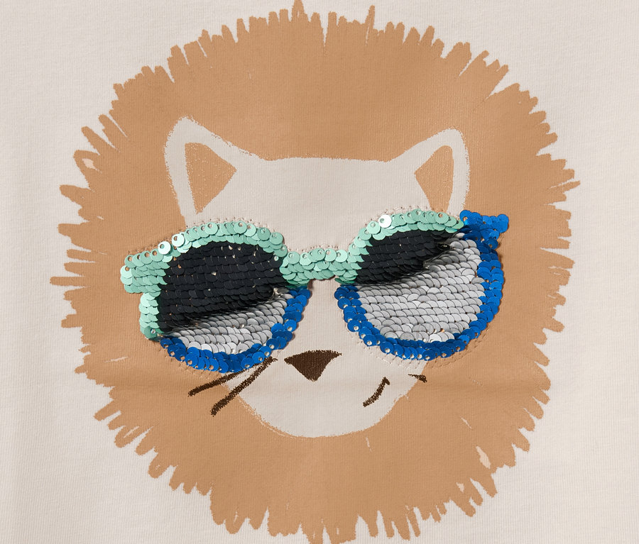 Gros plan sur un t-shirt pour enfant orné d'une tête de lion et de paillettes réversibles sur les lunettes de soleil.