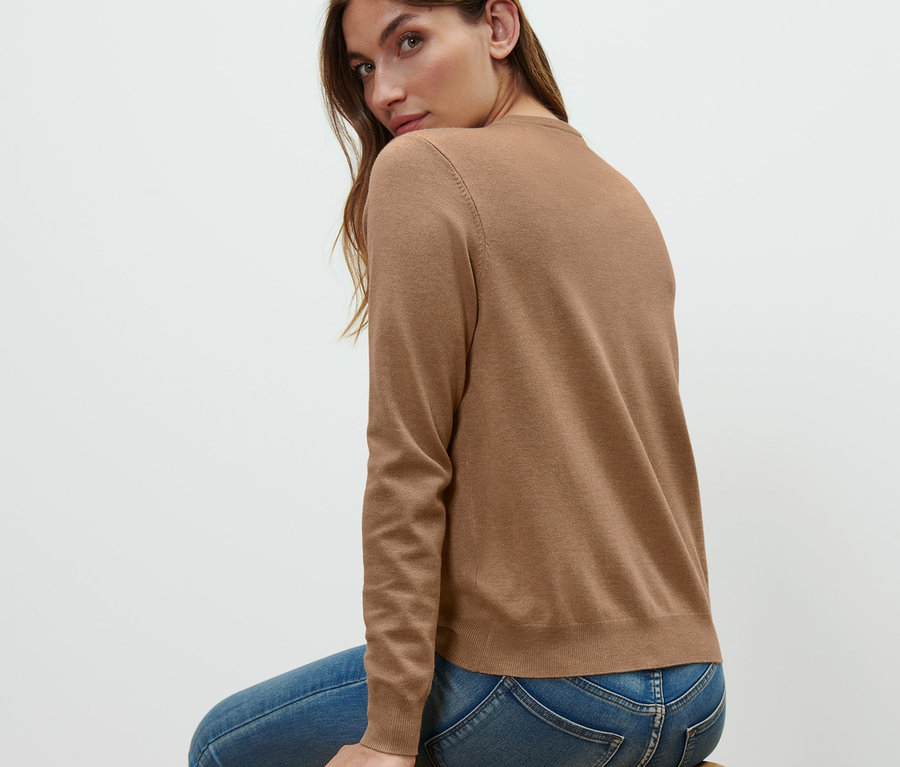 Femme assise sur un tabouret en bois portant un cardigan en maille fine.