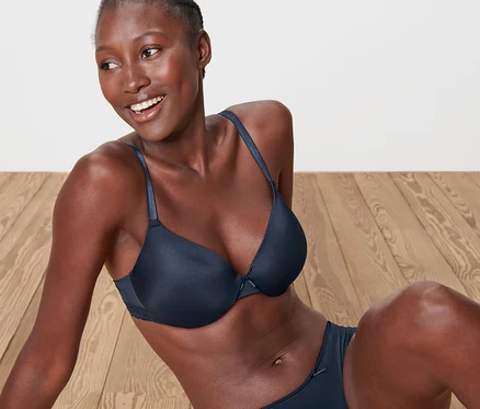 Une femme est assise sur un plancher en bois et porte un soutien-gorge invisible bleu et une culotte.