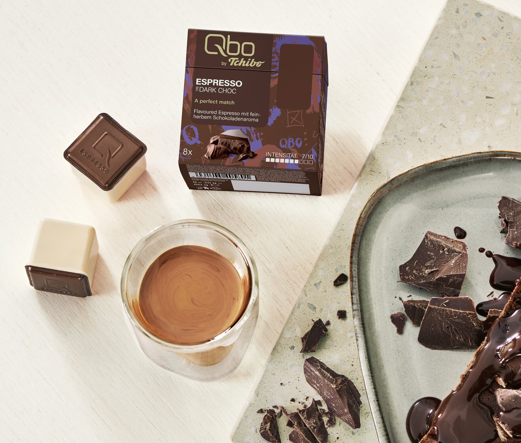 Une part de tarte au chocolat avec des capsules Qbo Flavoured Espresso Dark Choc et un expresso dans un verre.