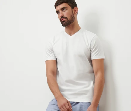 Un homme appuyé contre un mur portant un t-shirt blanc à col en V et un short bleu.