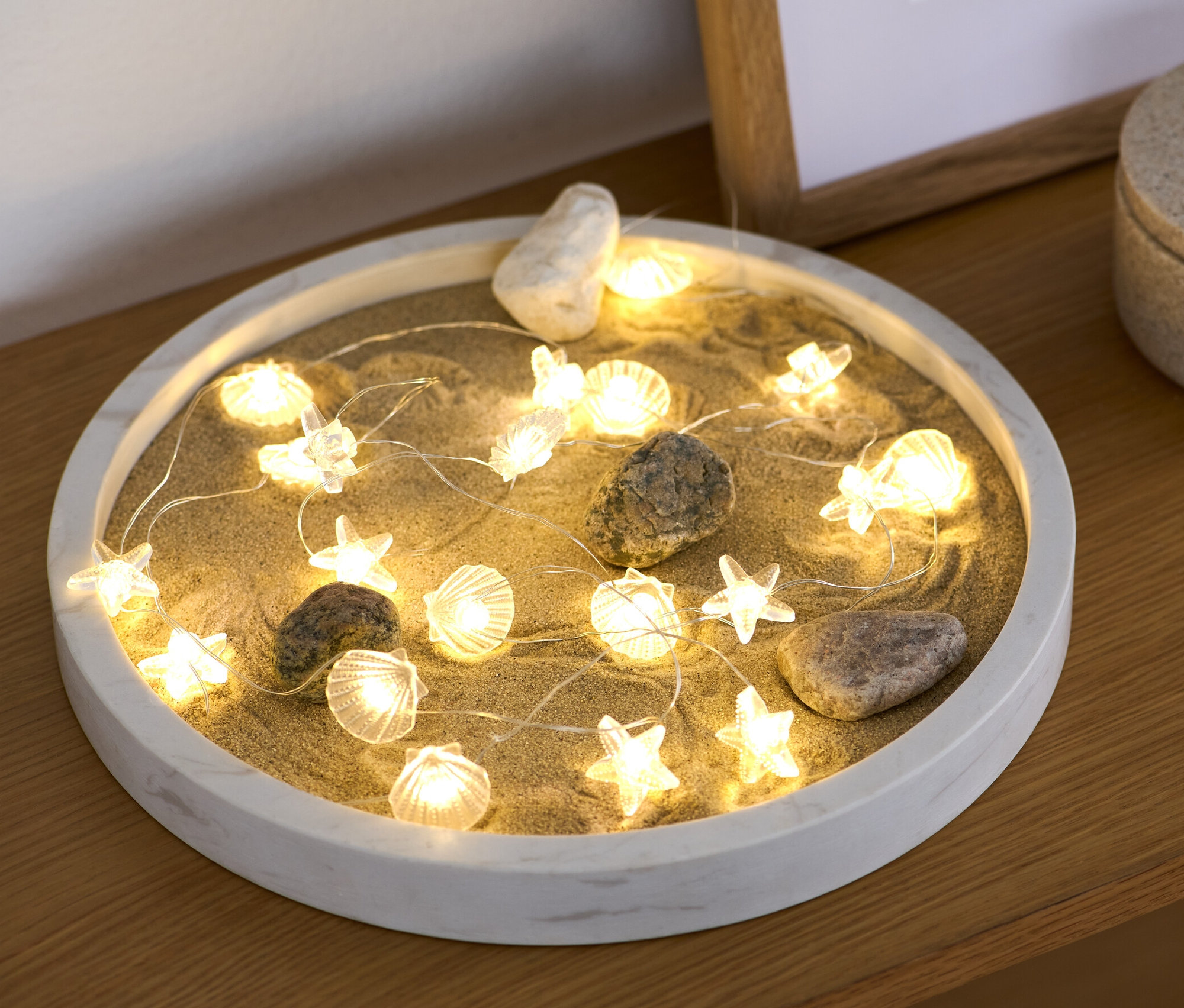 Micro-guirlande lumineuse LED « Coquillage » posée sur du sable dans un récipient décoratif.