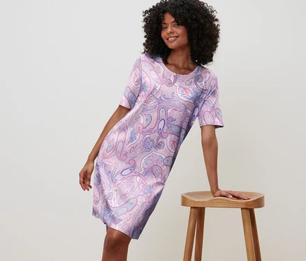 Femme appuyée sur un tabouret portant une chemise de nuit à motif floral.