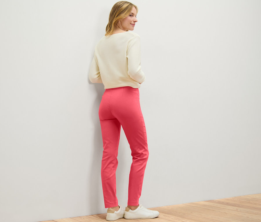 Une femme regarde par-dessus son épaule et porte un pantalon stretch corail.