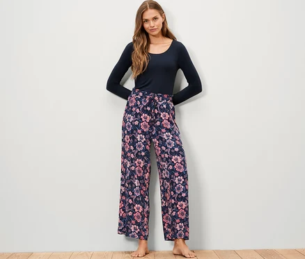 Une femme debout porte un pantalon relax tissé à motif floral et un haut bleu à manches longues.