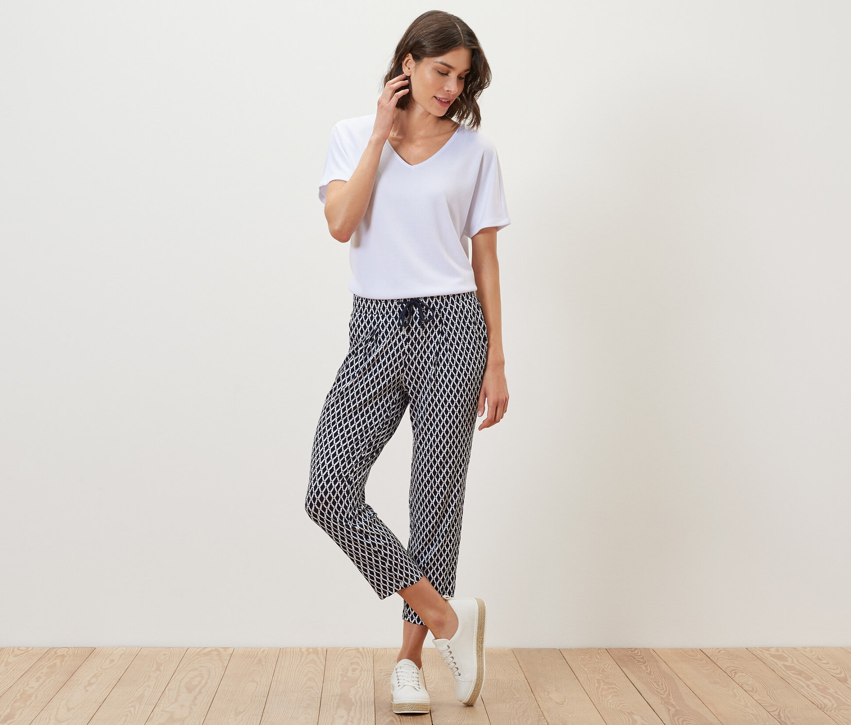 Femme posant en t-shirt blanc et pantalon en jersey imprimé.