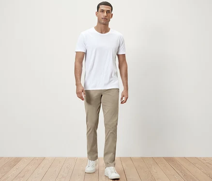 Un homme debout porte un t-shirt blanc et un pantalon chino beige.