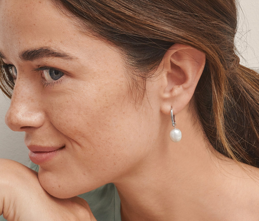 Portrait d'une femme aux cheveux bruns, le visage appuyé sur sa main. Elle porte des créoles en argent 925 rhodié avec des perles de culture d'eau douce.