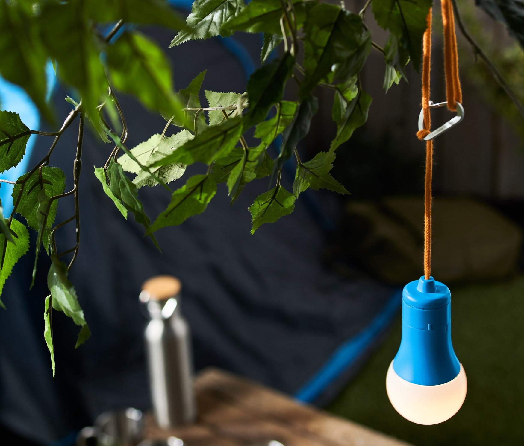 Une lampe de camping à LED bleue est suspendue à une branche d'arbre, avec une tente en arrière-plan.