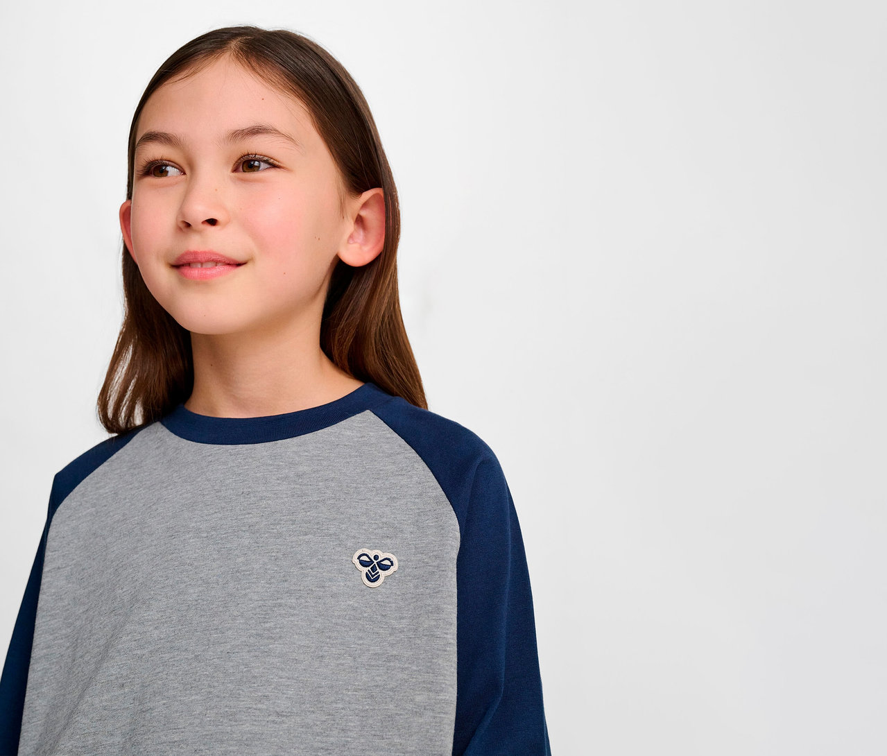 Portrait d'une jeune fille portant un t-shirt ample à manches raglan HUMMEL HMLJR BEE bleu et gris.