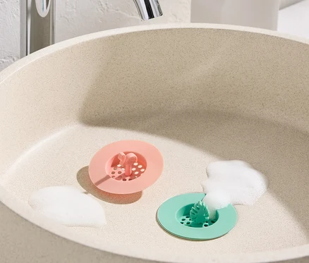 Lavabo avec 2 tamis d’évier en silicone roses et verts et de la mousse.