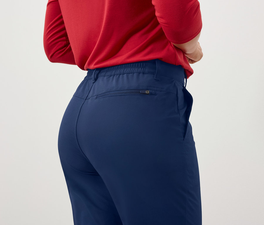 Une femme dos à la caméra porte un haut rouge à manches longues et un pantalon bleu.