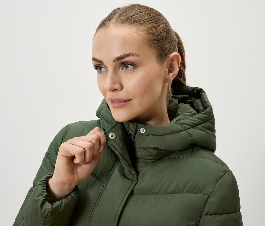 Femme fermant une doudoune vert olive à capuche.