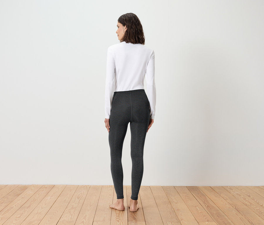 Une femme, vue de dos, porte un T-shirt blanc à manches longues et un legging gris.