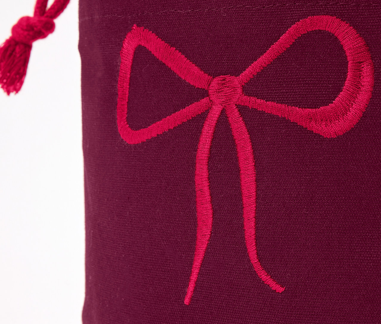 Gros plan sur un sac cadeau bordeaux avec un nœud rouge.