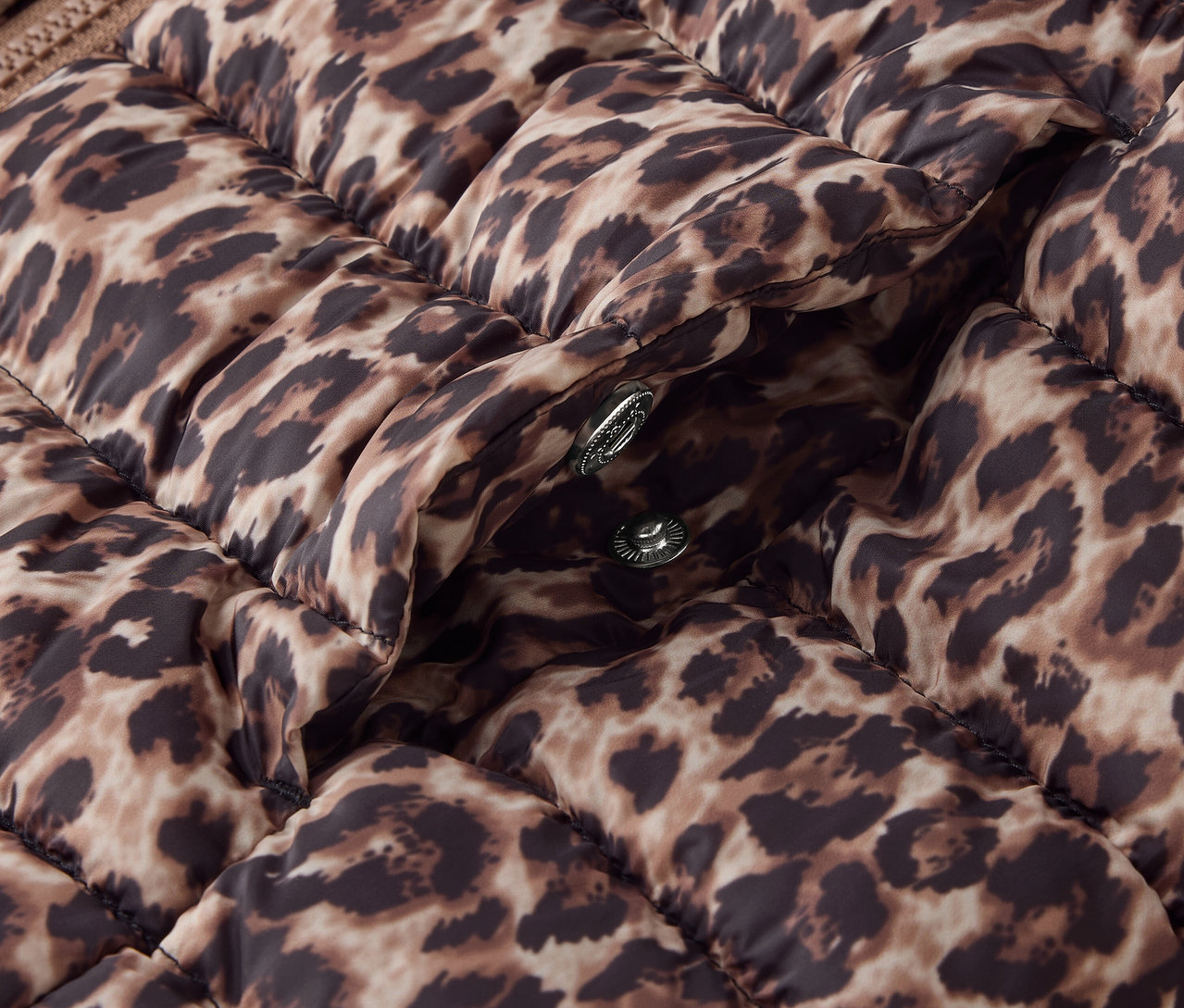 Détail d'une doudoune marron matelassée avec un imprimé animal et des boutons-pression argentés.