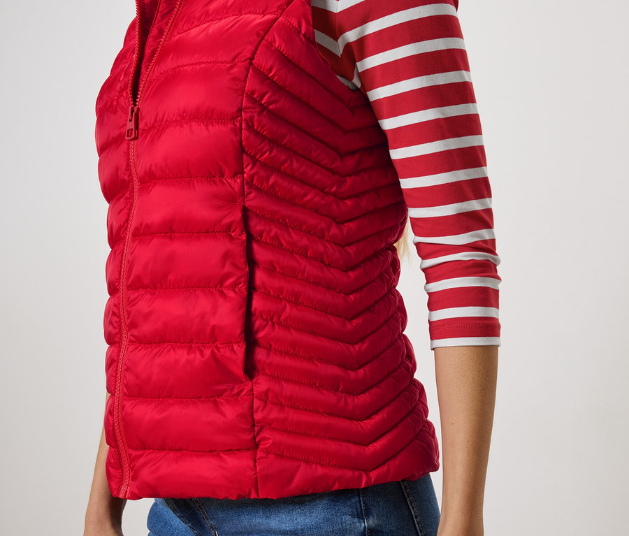 Vue partielle d'une femme portant une veste sans manches rouge matelassée et un t-shirt rayé.