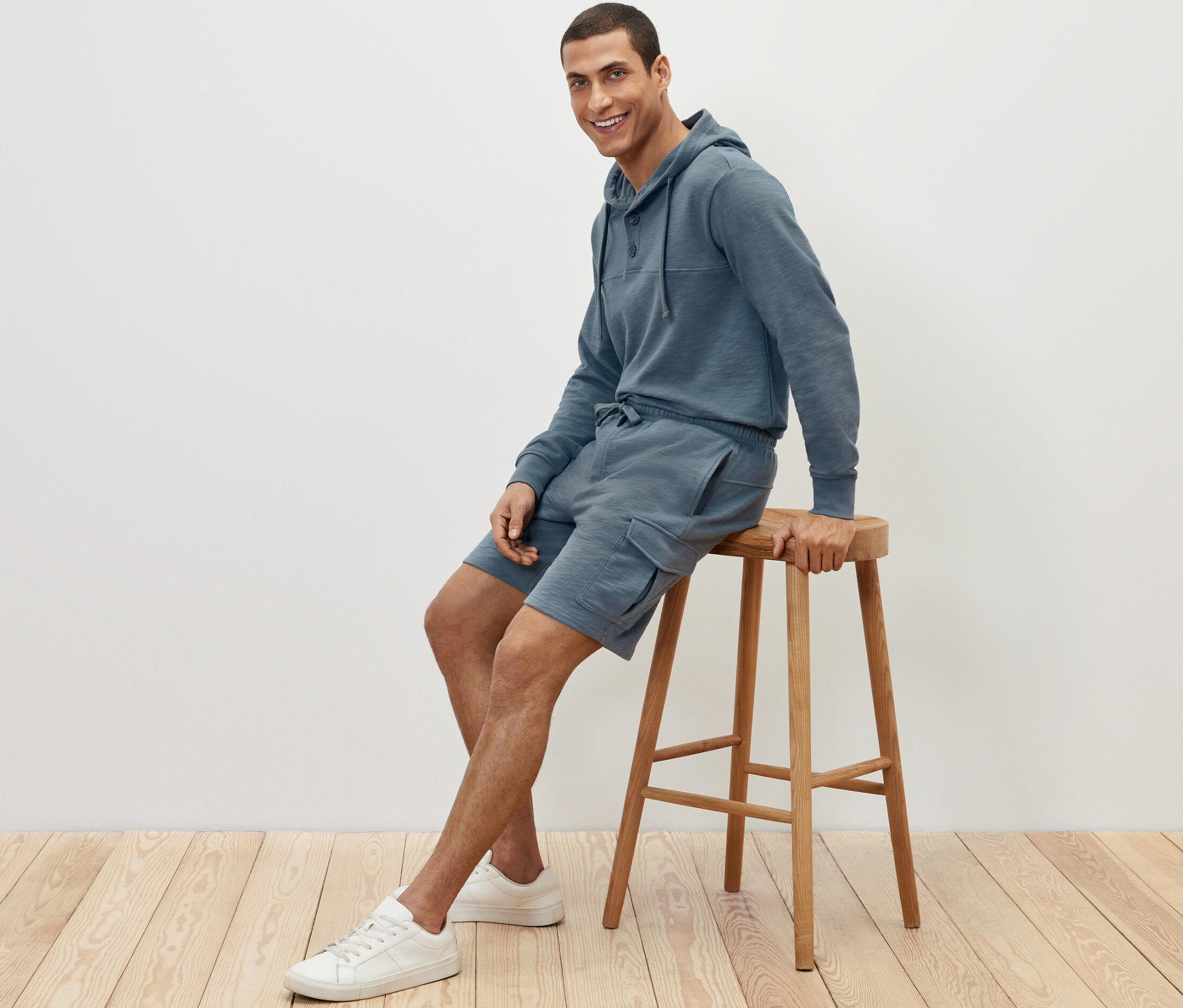 Un homme est assis sur un tabouret et porte un short cargo en sweat et un sweat à capuche.
