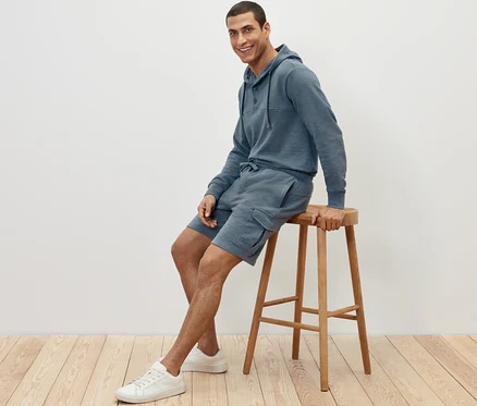 Un homme est assis sur un tabouret et porte un short cargo en sweat et un sweat à capuche.