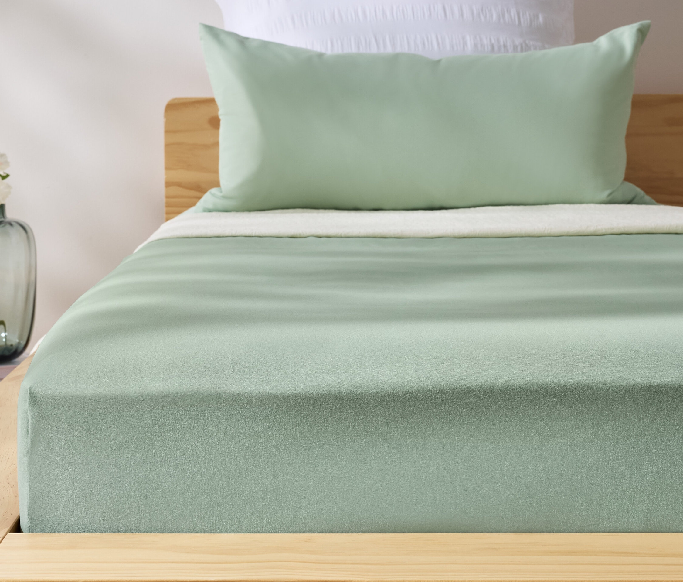 Drap-housse vert en microfibre sur un lit. Un vase avec des fleurs est à côté du lit.