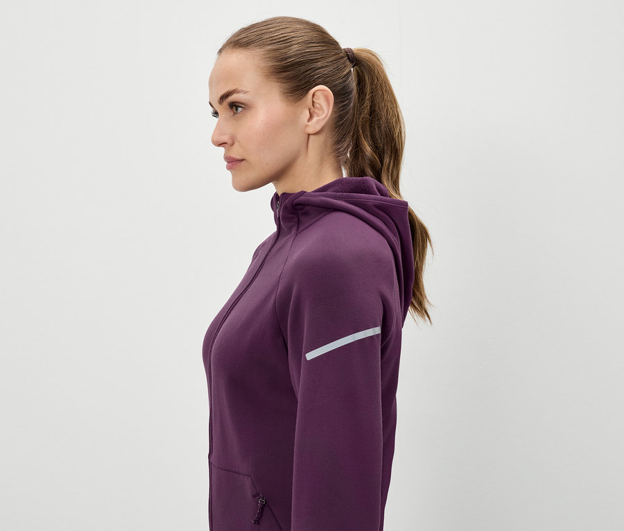Profil d'une femme aux cheveux bruns attachés en queue de cheval, elle porte un sweat à capuche violet.