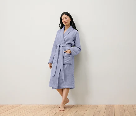 Une femme debout porte un peignoir violet clair.