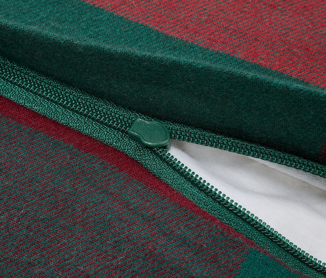 Gros plan sur la fermeture éclair d'une housse de coussin à carreaux verts et rouges, révélant un rembourrage intérieur blanc.