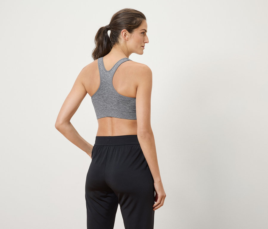 Une femme porte un soutien-gorge de sport gris et un pantalon noir.