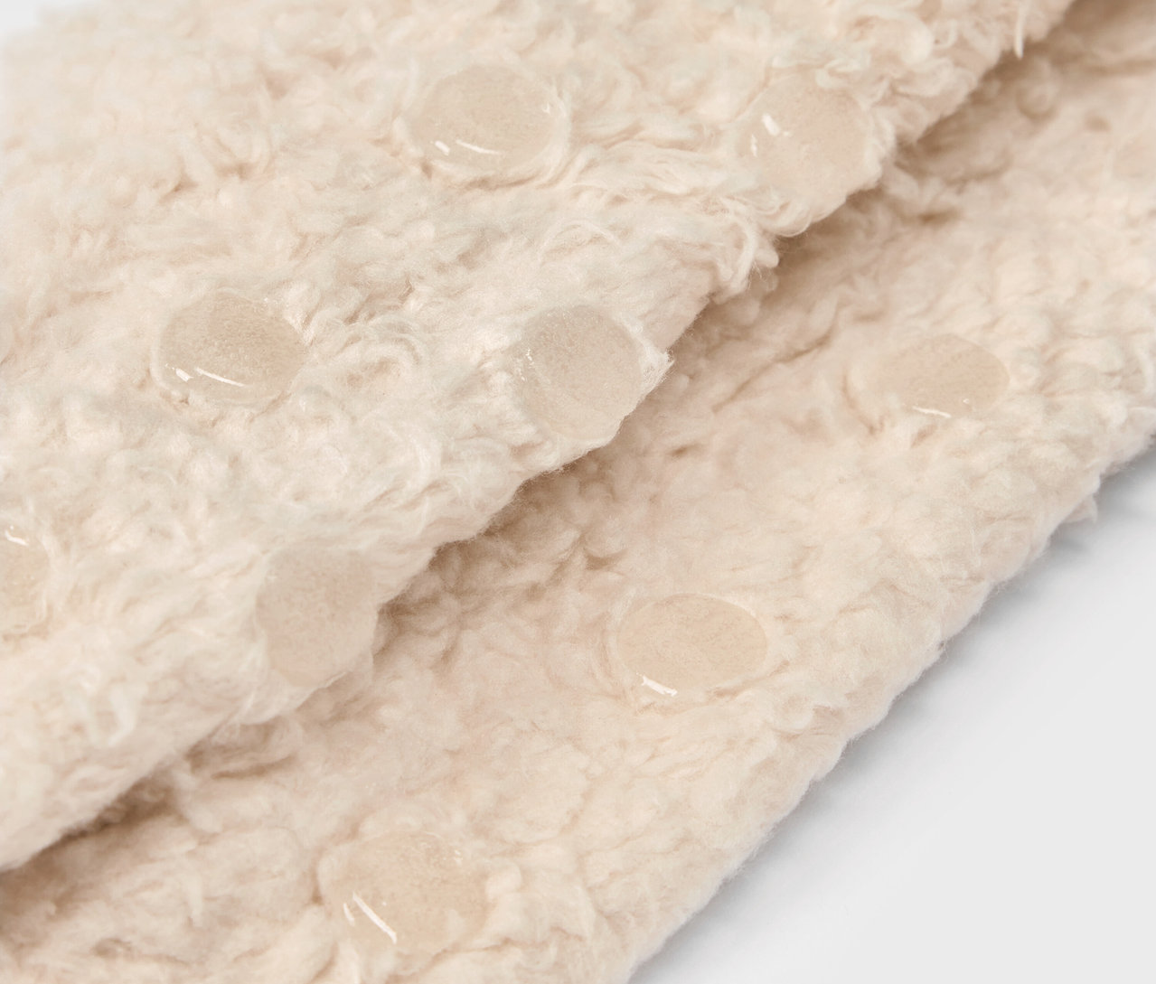 Gros plan sur un tissu beige duveteux avec des éléments antidérapants.