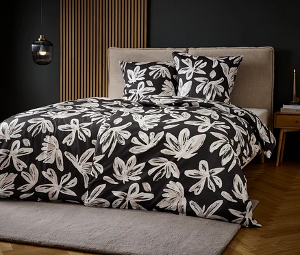 Lit avec literie à motif floral noir et blanc sur un tapis gris.