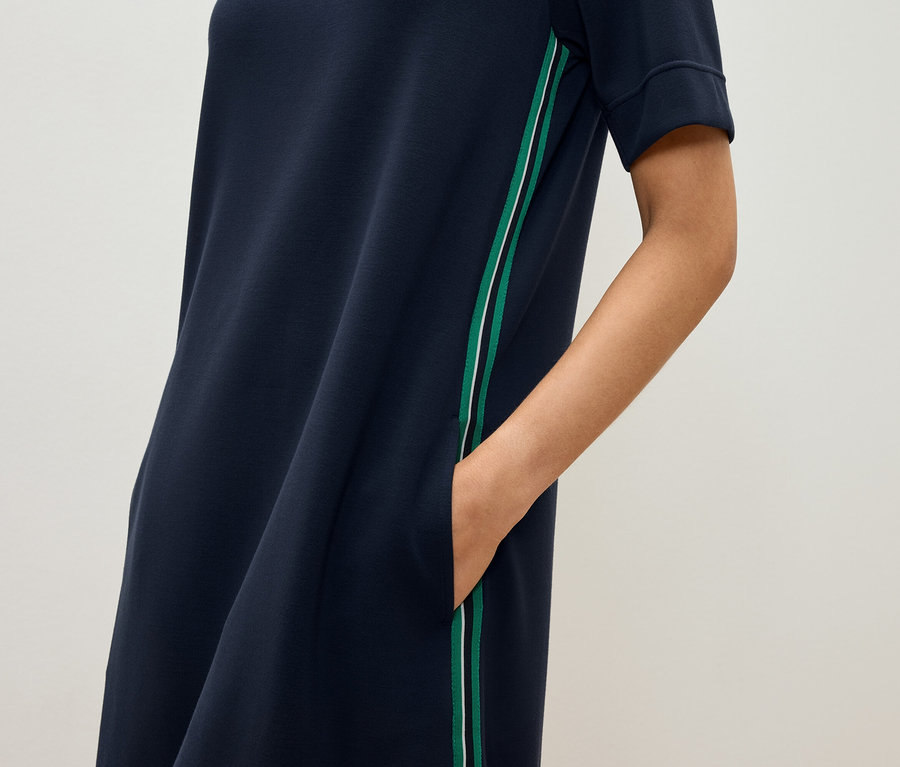 Une femme a la main dans la poche d'une robe bleu marine à manches courtes avec une rayure verte et blanche.