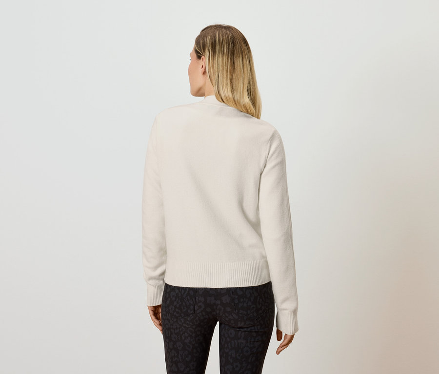 Vue arrière d'une femme blonde portant un pull crème et un legging noir.