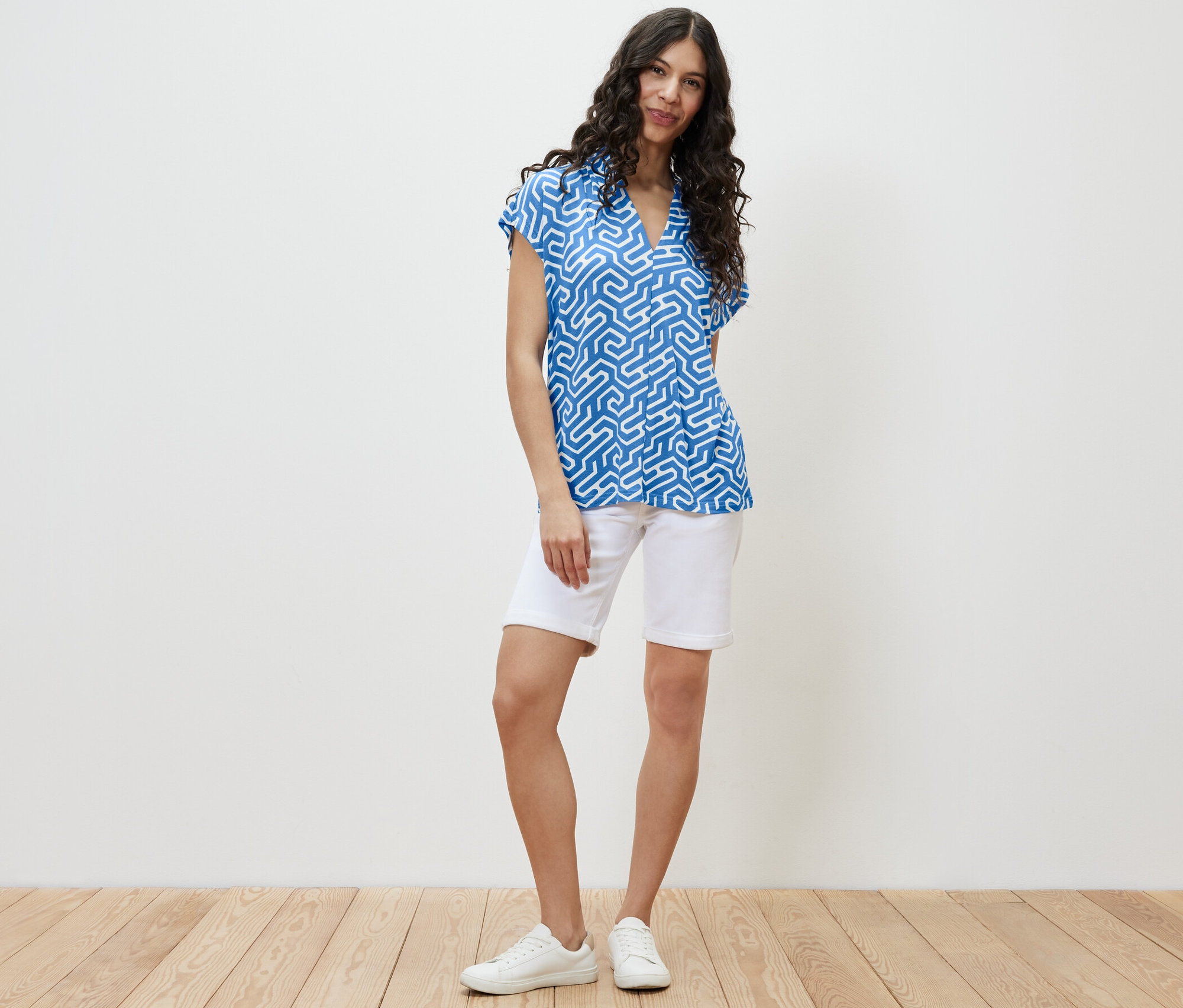 Une femme debout portant une blouse bleue à encolure en V et un short blanc.