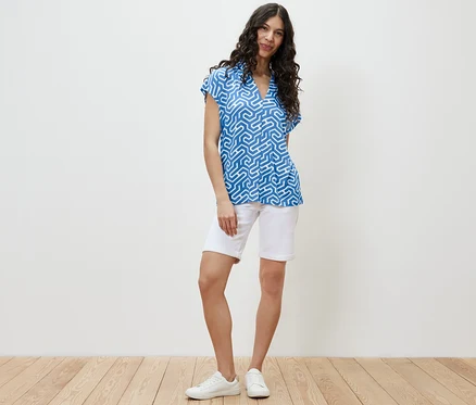 Une femme debout portant une blouse bleue à encolure en V et un short blanc.