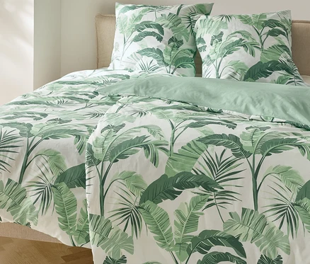 Lit avec parure de lit en renforcé à motif de palmiers et deux oreillers.